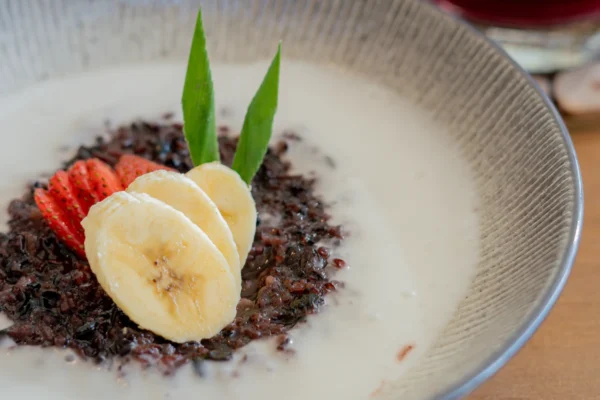 Black sticky rice porridge with coconut milk sauce and banana & strawberry on top