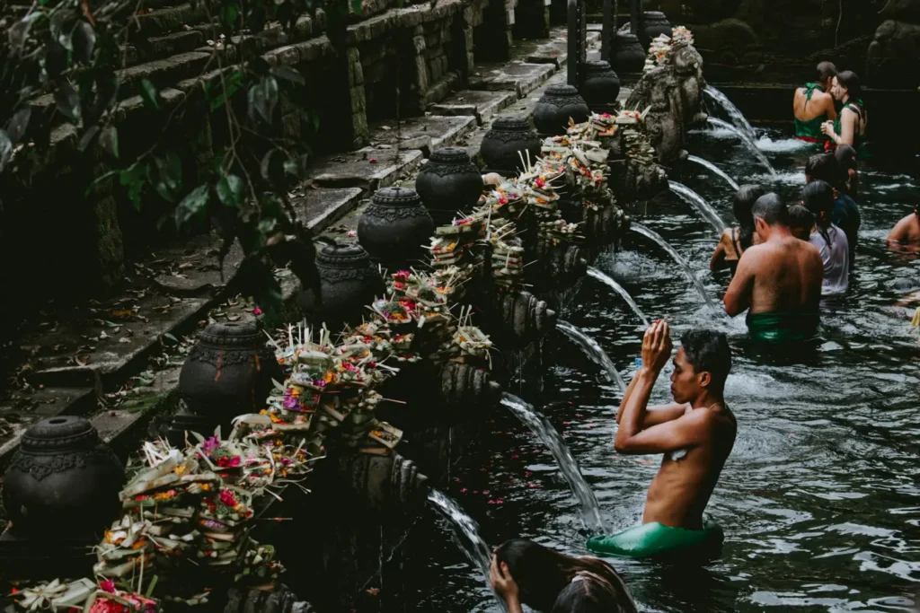 People performing a Balinese temple ritual, bathing under water spouts surrounded by traditional offerings